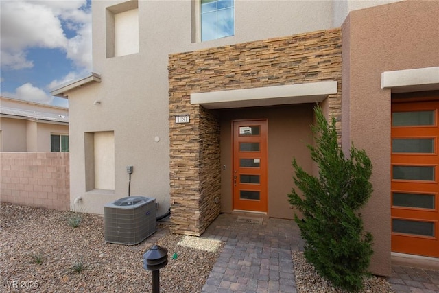 entrance to property with stone siding, stucco siding, and central AC