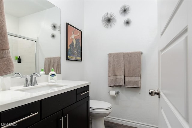 bathroom featuring a shower with shower door, toilet, wood finished floors, baseboards, and vanity