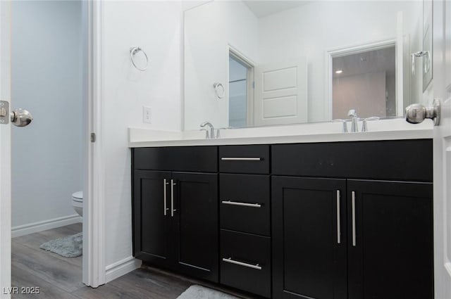 full bathroom featuring toilet, a sink, wood finished floors, double vanity, and baseboards