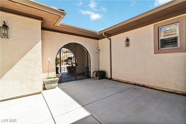 entrance to property featuring a gate, a patio area, and stucco siding