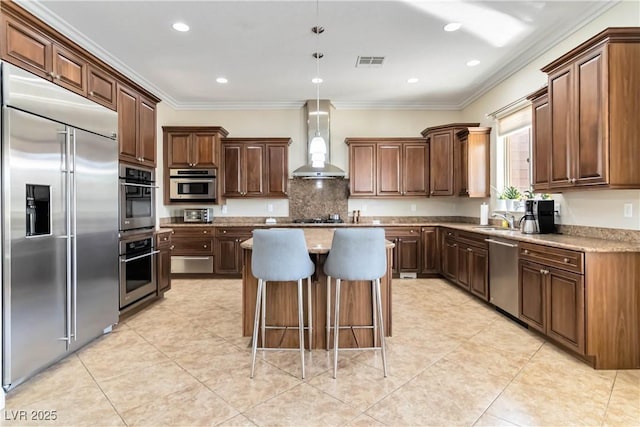 kitchen with a kitchen island, crown molding, wall chimney range hood, appliances with stainless steel finishes, and a sink