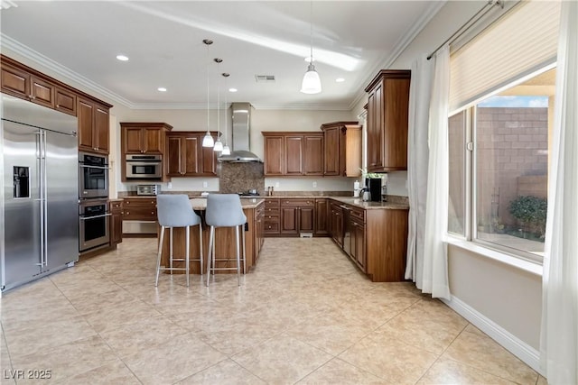 kitchen featuring visible vents, ornamental molding, a kitchen island, stainless steel appliances, and wall chimney exhaust hood