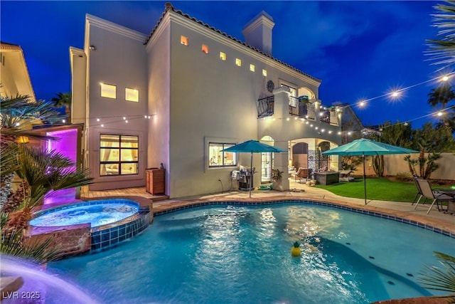 pool at night featuring a pool with connected hot tub and a patio