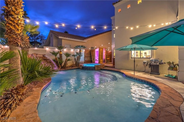 pool at night featuring a patio area, a grill, and a pool with connected hot tub