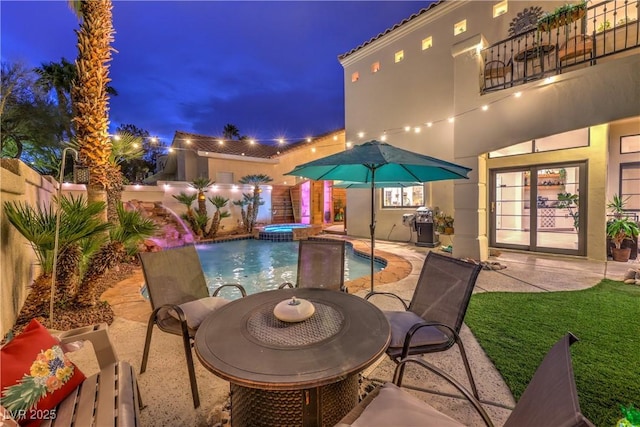 pool at night with a patio, an in ground hot tub, and fence