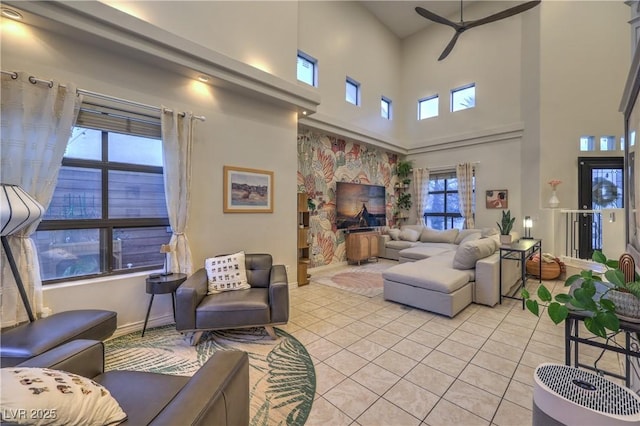 living room featuring light tile patterned floors, baseboards, a ceiling fan, and a towering ceiling