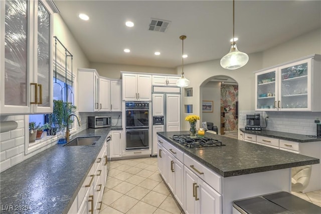 kitchen with visible vents, a center island, white cabinets, stainless steel appliances, and a sink