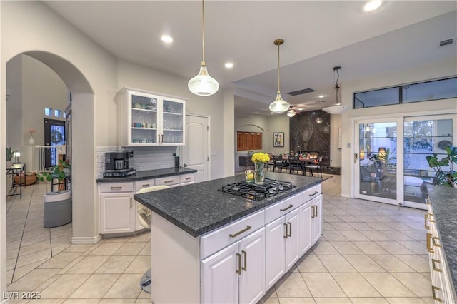 kitchen with decorative light fixtures, glass insert cabinets, gas stovetop, arched walkways, and decorative backsplash