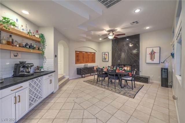 dining area featuring visible vents, arched walkways, light tile patterned flooring, a fireplace, and ceiling fan