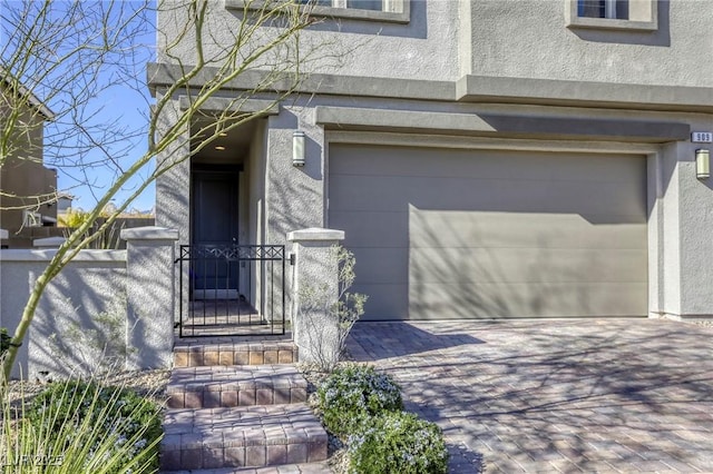 doorway to property with stucco siding, decorative driveway, a garage, and fence