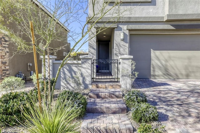 entrance to property with a gate, stucco siding, decorative driveway, and fence