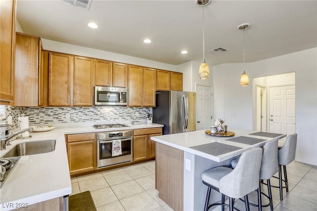 kitchen featuring a breakfast bar area, appliances with stainless steel finishes, light tile patterned flooring, brown cabinetry, and a sink