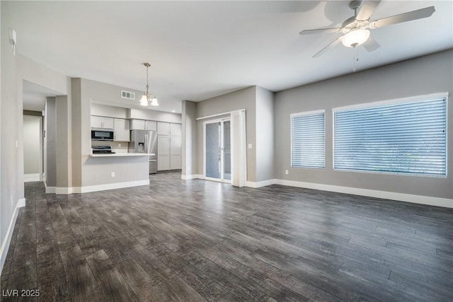 unfurnished living room with dark wood finished floors, visible vents, ceiling fan with notable chandelier, and baseboards