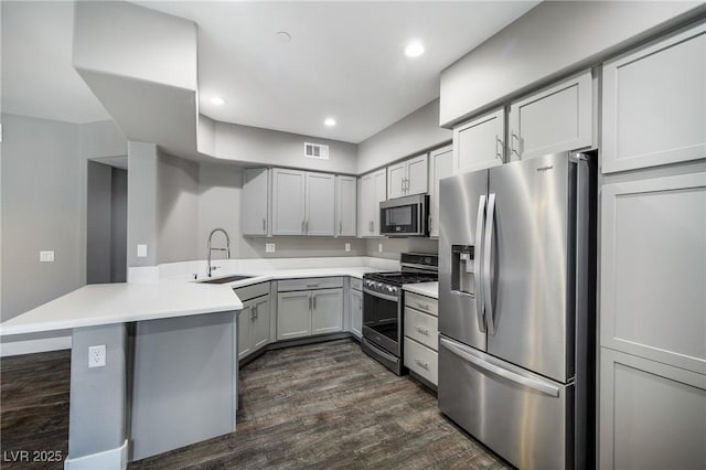 kitchen featuring dark wood-style floors, a peninsula, a sink, stainless steel appliances, and light countertops