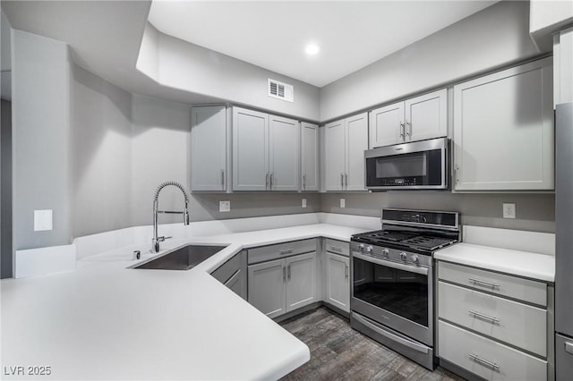 kitchen with visible vents, a sink, stainless steel appliances, dark wood-type flooring, and light countertops