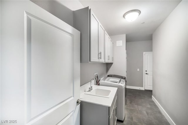 washroom with washing machine and dryer, cabinet space, baseboards, and a sink