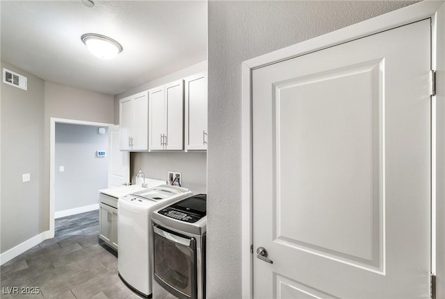 kitchen with visible vents, a sink, white cabinets, baseboards, and washing machine and clothes dryer