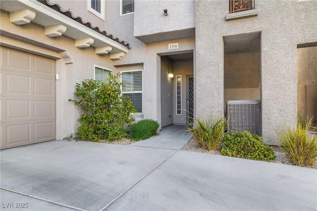 property entrance featuring a garage, a tile roof, central AC, and stucco siding