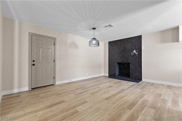 unfurnished living room featuring baseboards, visible vents, light wood finished floors, and a large fireplace