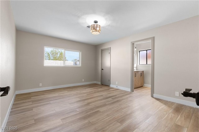 unfurnished bedroom featuring light wood-type flooring, baseboards, visible vents, and ensuite bath