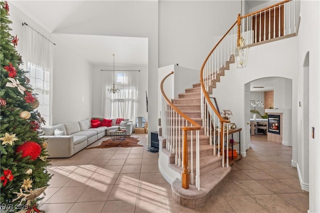 interior space with a tiled fireplace, a chandelier, stairs, light tile patterned floors, and a high ceiling