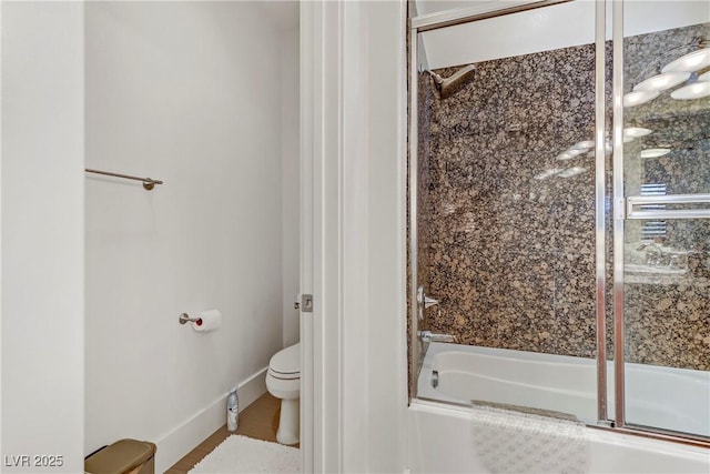 bathroom featuring combined bath / shower with glass door, baseboards, and toilet