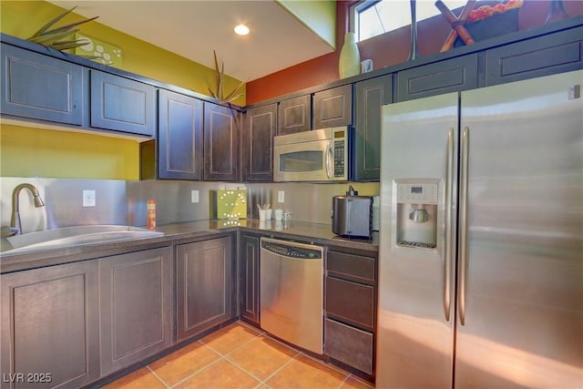 kitchen featuring light tile patterned floors, recessed lighting, a sink, stainless steel appliances, and dark countertops