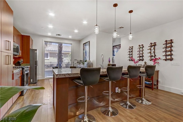 kitchen with visible vents, stainless steel appliances, light wood-style floors, a kitchen breakfast bar, and brown cabinets