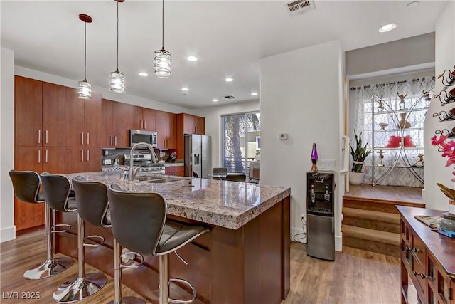 kitchen featuring visible vents, a kitchen bar, light wood-style flooring, a sink, and appliances with stainless steel finishes