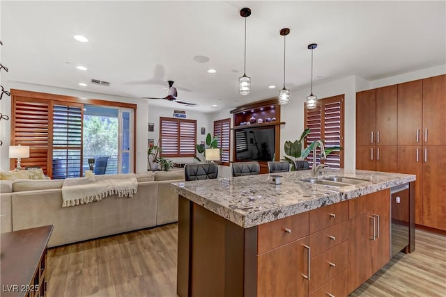 kitchen with visible vents, pendant lighting, a sink, open floor plan, and light wood-style floors