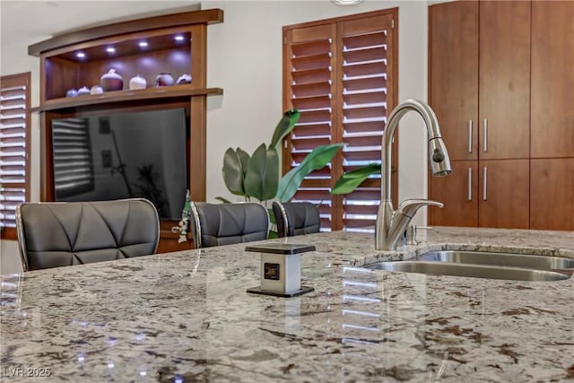 kitchen featuring a sink, light stone counters, and brown cabinetry