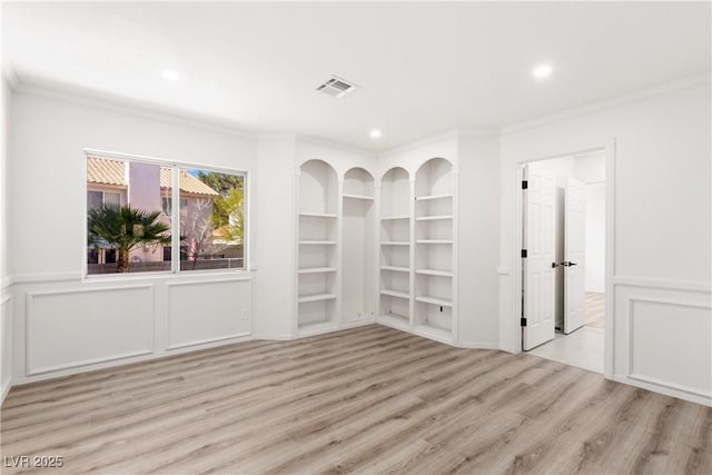 unfurnished room featuring crown molding, a decorative wall, built in shelves, and wood finished floors