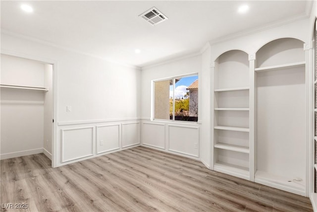 unfurnished bedroom with light wood finished floors, visible vents, crown molding, a wainscoted wall, and a decorative wall