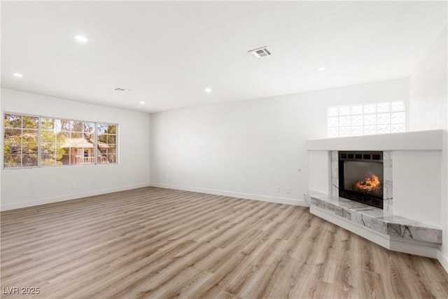 unfurnished living room featuring a high end fireplace, visible vents, light wood-style flooring, and baseboards