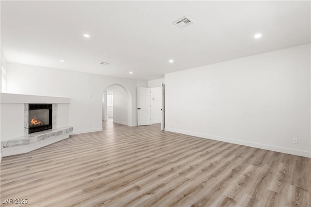 unfurnished living room featuring visible vents, arched walkways, light wood-style floors, and baseboards