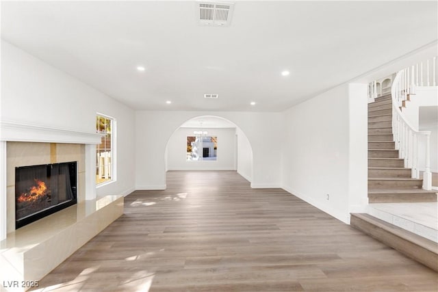 unfurnished living room with visible vents, stairs, a fireplace, light wood-style floors, and arched walkways