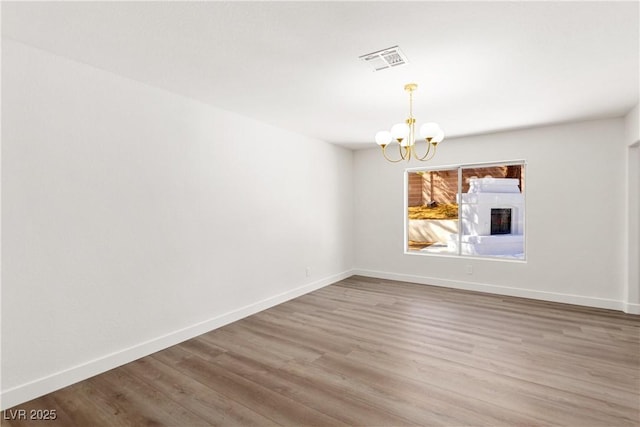 spare room featuring visible vents, baseboards, an inviting chandelier, and wood finished floors