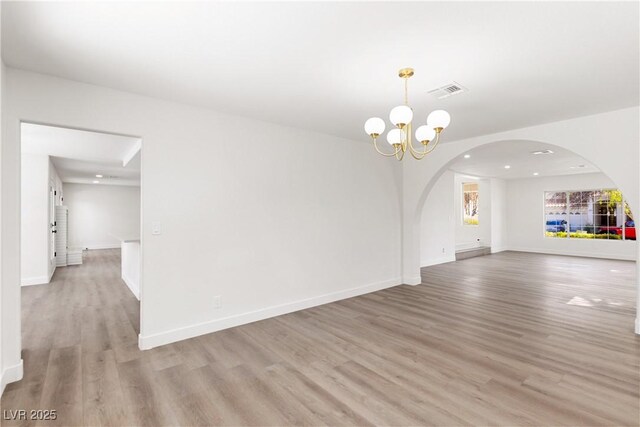 empty room featuring visible vents, baseboards, a chandelier, and light wood finished floors