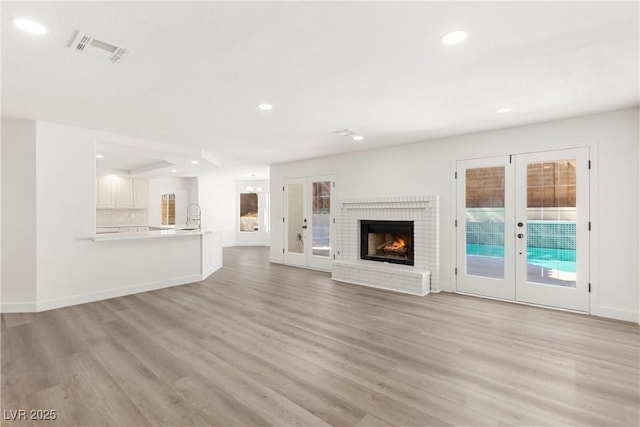 unfurnished living room featuring light wood-type flooring, visible vents, recessed lighting, french doors, and baseboards