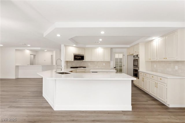 kitchen with a sink, a raised ceiling, light wood-style floors, and recessed lighting