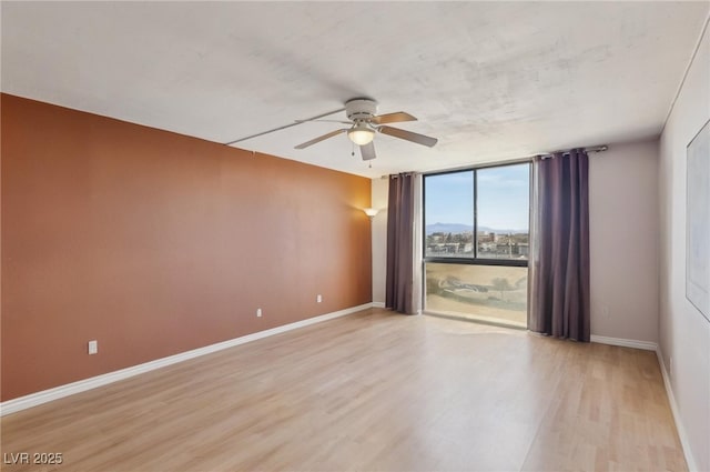 unfurnished room featuring a wall of windows, baseboards, light wood finished floors, and ceiling fan