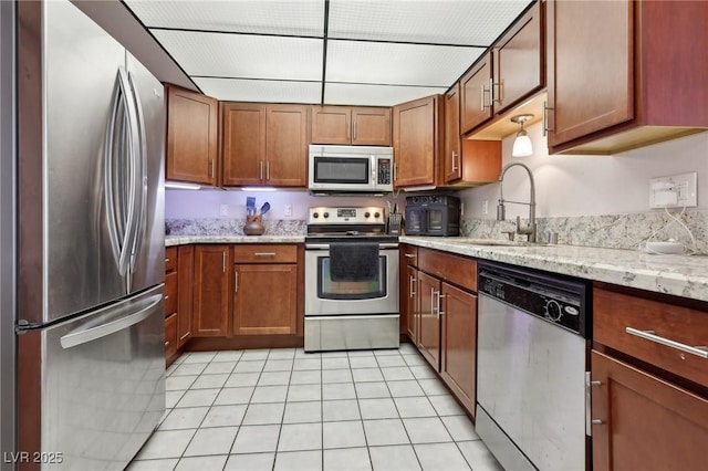 kitchen featuring a sink, light stone counters, stainless steel appliances, brown cabinetry, and light tile patterned floors