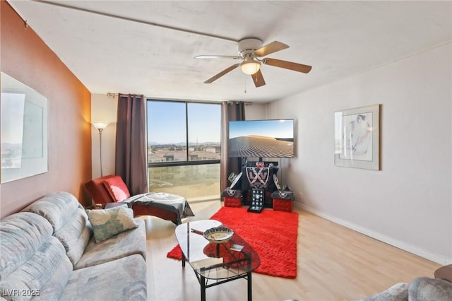 living room featuring ceiling fan, expansive windows, baseboards, and wood finished floors