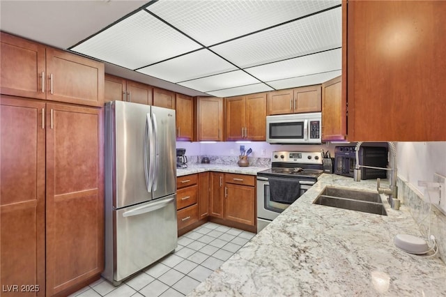 kitchen featuring brown cabinets, light stone counters, a sink, stainless steel appliances, and light tile patterned floors