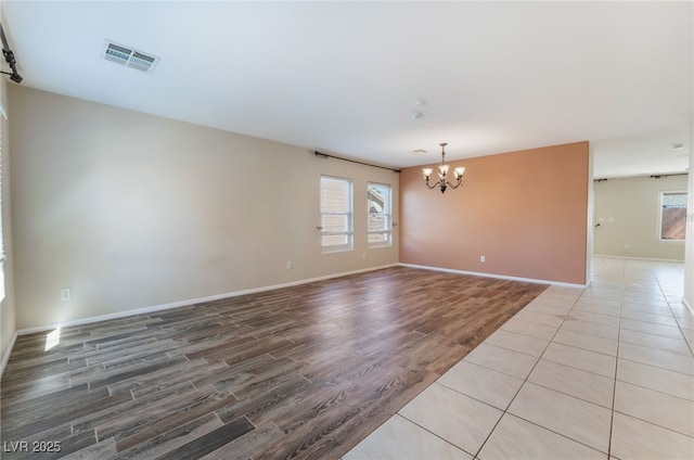 empty room featuring baseboards, wood finished floors, visible vents, and a chandelier