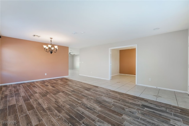 unfurnished room with visible vents, baseboards, a notable chandelier, and wood finished floors