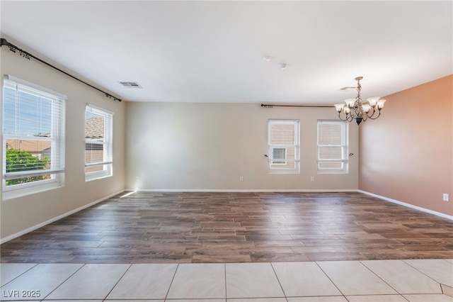 spare room with baseboards, wood finished floors, visible vents, and a chandelier