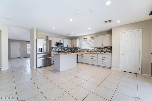 kitchen with a sink, tasteful backsplash, a center island, appliances with stainless steel finishes, and light tile patterned floors