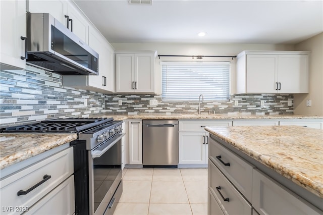 kitchen with light tile patterned flooring, a sink, stainless steel appliances, white cabinets, and backsplash