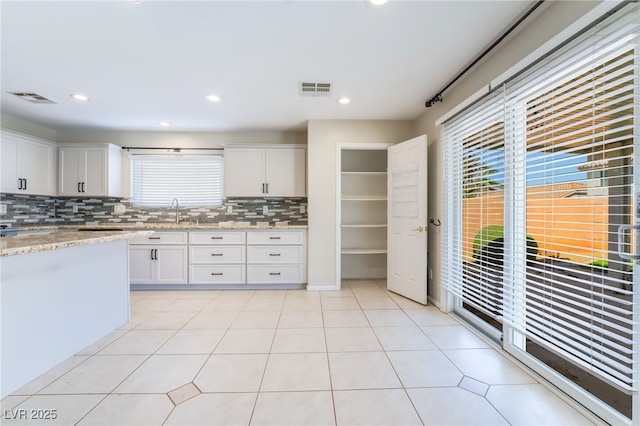 kitchen with visible vents, a sink, tasteful backsplash, white cabinetry, and light tile patterned floors